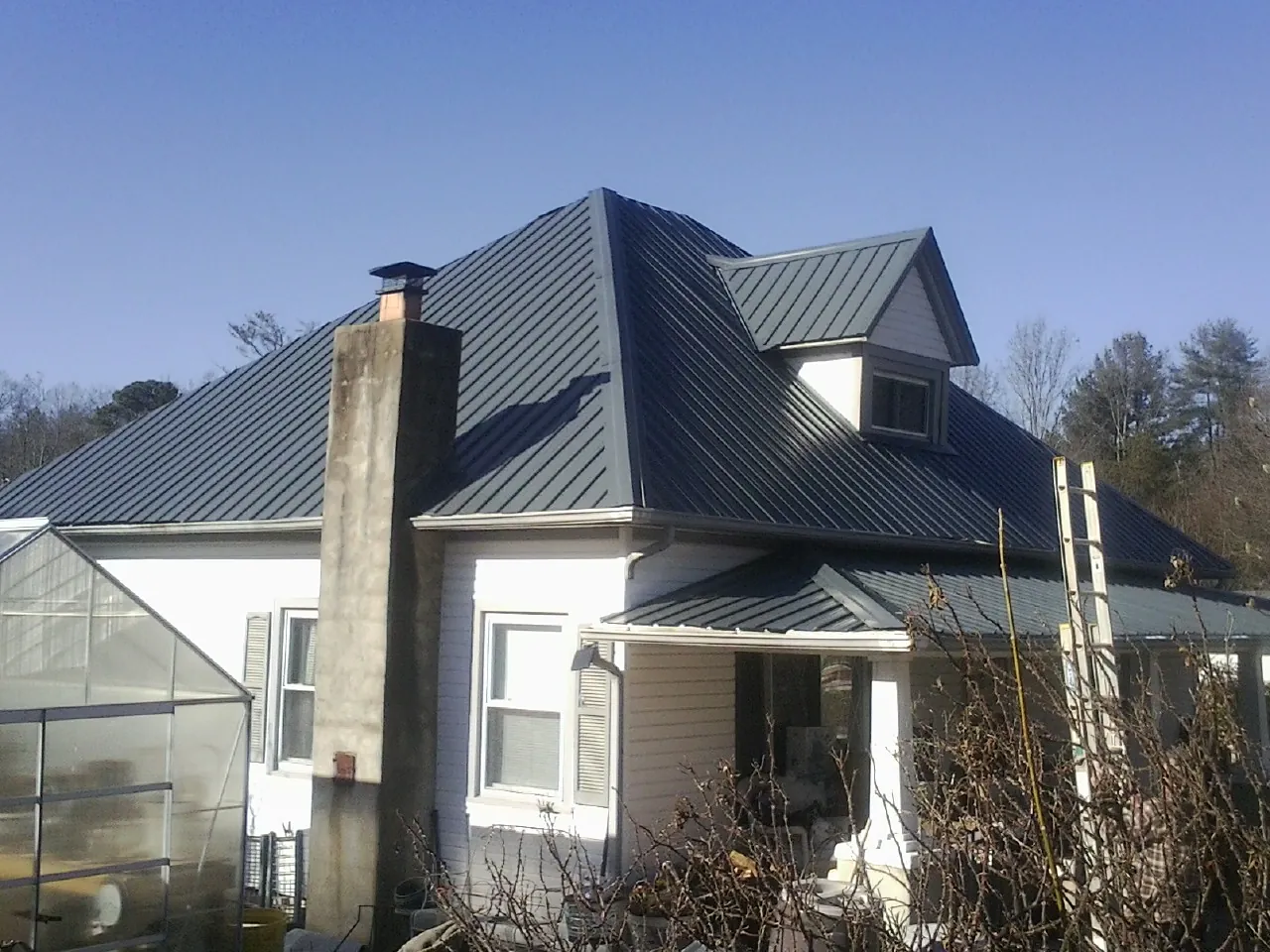 Dark blue standing seam metal roof on a white farmhouse with dormer — Slate & Tile Roof Repair by Roofing Brothers in Hollister