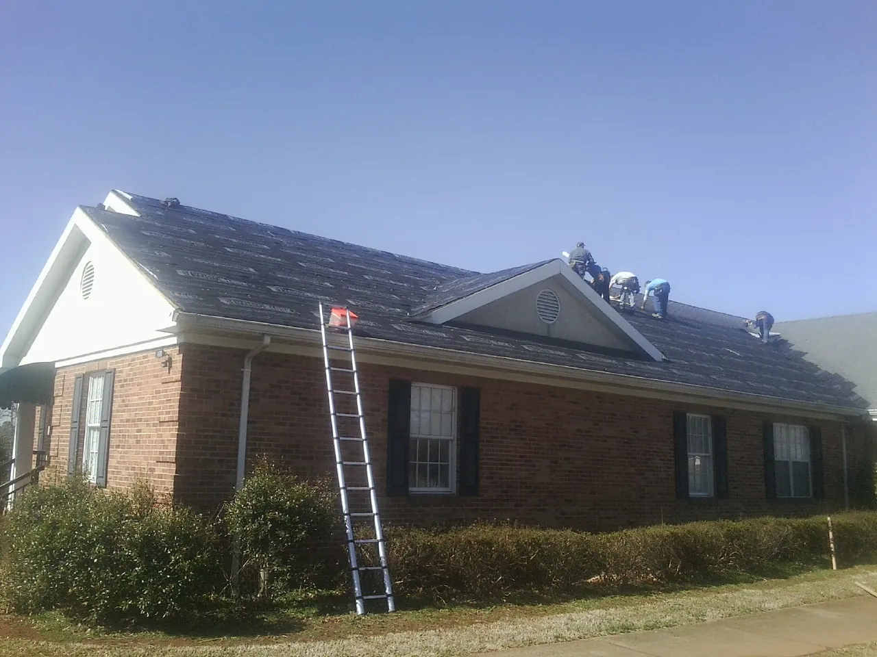 Crew tearing shingles off a brick ranch roof with a ladder set — Emergency Roof Repair work by our crew in Hollister