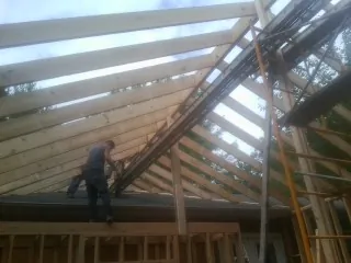 Rafters going up over a new addition with a worker on the wall in Hollister