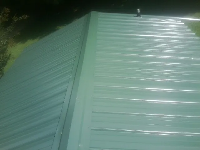 New green metal panels meeting at the ridge of a roof — Flat Roof Repair work by our crew in Hollister