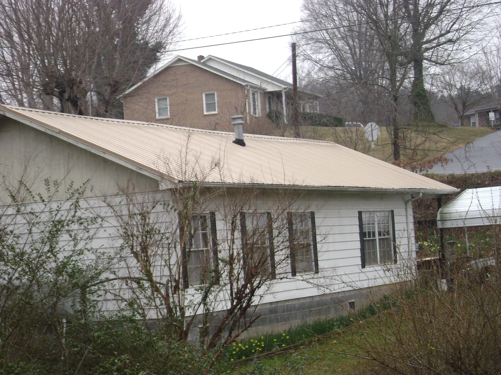 Tan metal roof on a white sided house set into a hillside — Commercial Roofing by Roofing Brothers in Hollister